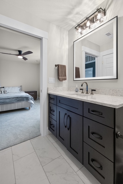 A guest ensuite bath with dark vanity, stone counter and marble tile, opening onto the bedroom