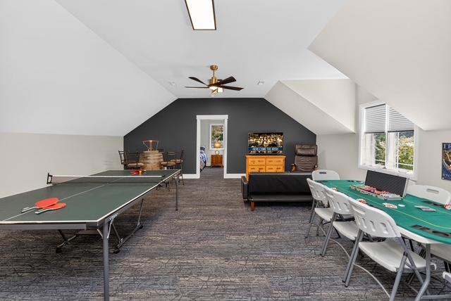 The upstairs game room with a ping pong table, poker table and lounge seating under vaulted ceilings