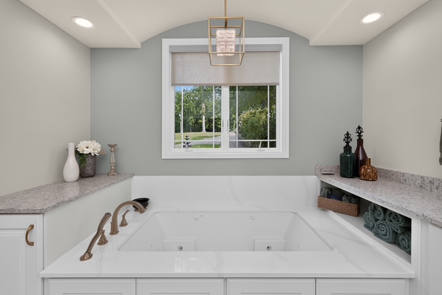 The primary bath soaking tub beneath a window, framed by stone counters and a lantern pendant