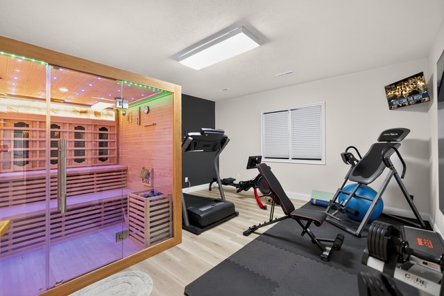 The private gym with treadmill, bench, weights and inversion table beside a glass-front infrared sauna