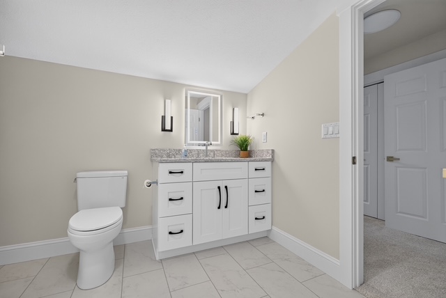 A guest bathroom with marble tile floor, stone-top vanity and backlit mirror