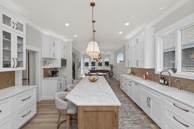 The full length of the chef’s kitchen, with the marble island, twin runs of cabinetry and the dining room beyond