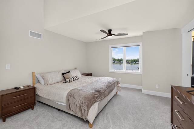 A light guest bedroom with a queen bed, walnut nightstands and a window framing the lake