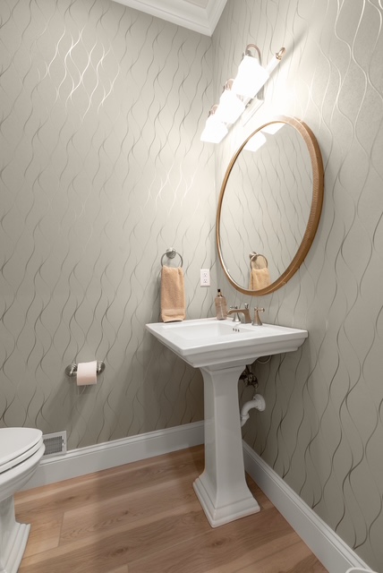 A powder room with textured wallcovering, pedestal sink and round brass mirror