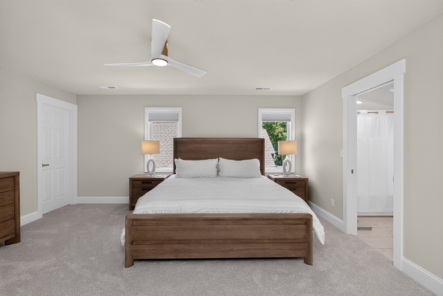 A neutral king guest bedroom with a wood bed frame, matched nightstands and an ensuite bath