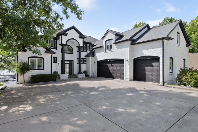 Ground-level view of the estate's white brick front elevation, columned entry and garages off the courtyard drive