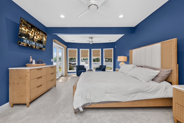 A lakefront guest suite in deep navy with a king bed, sitting chairs and doors onto the lake-facing balcony